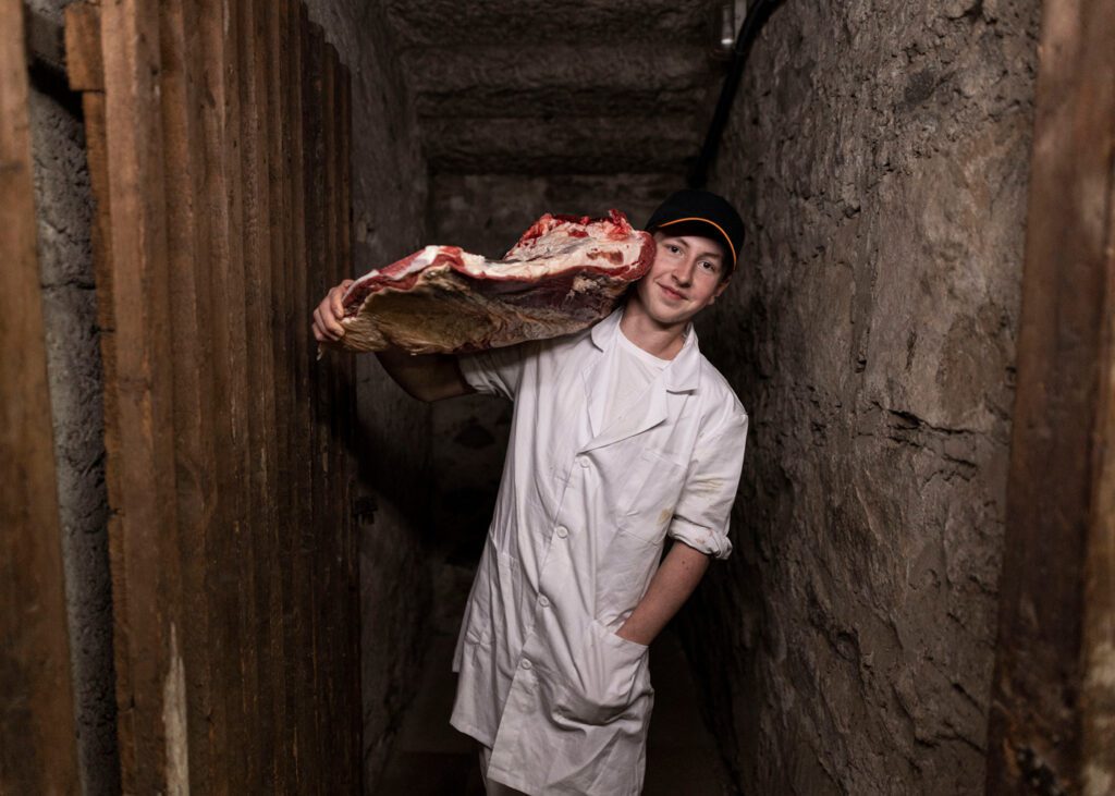 Metzgerlehrling im Keller, hält ein großes Fleischstück auf seinen Schultern